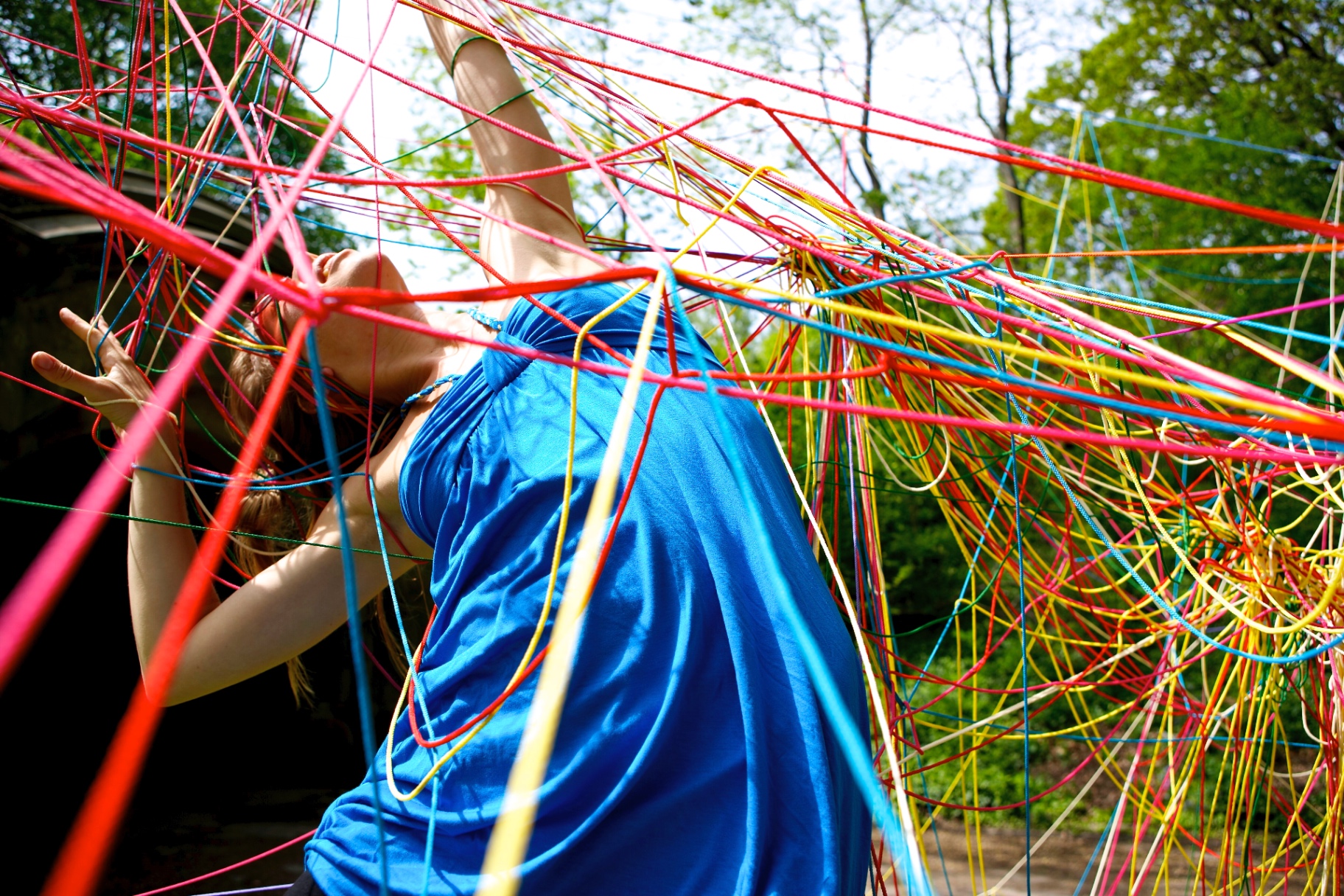 Woman in a blue dress leaning into a wall of colored strings