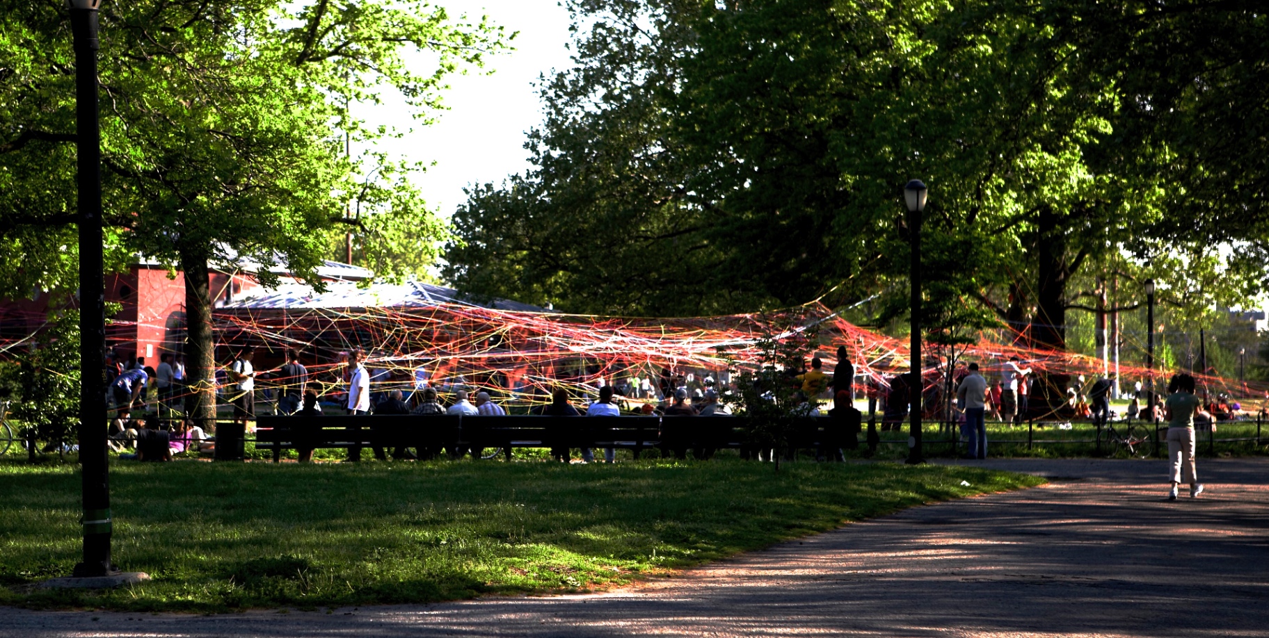 Wide view of a red and orange string web installation across McCarren Park